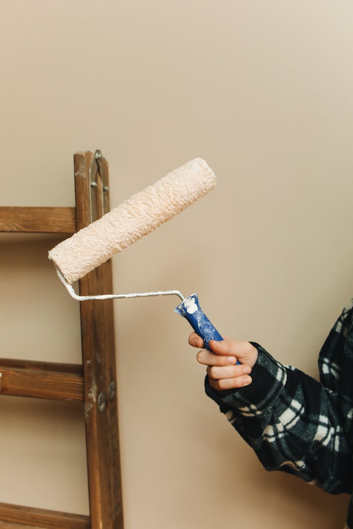 Close-up of a hand holding a paint roller next to a wooden ladder indoors.