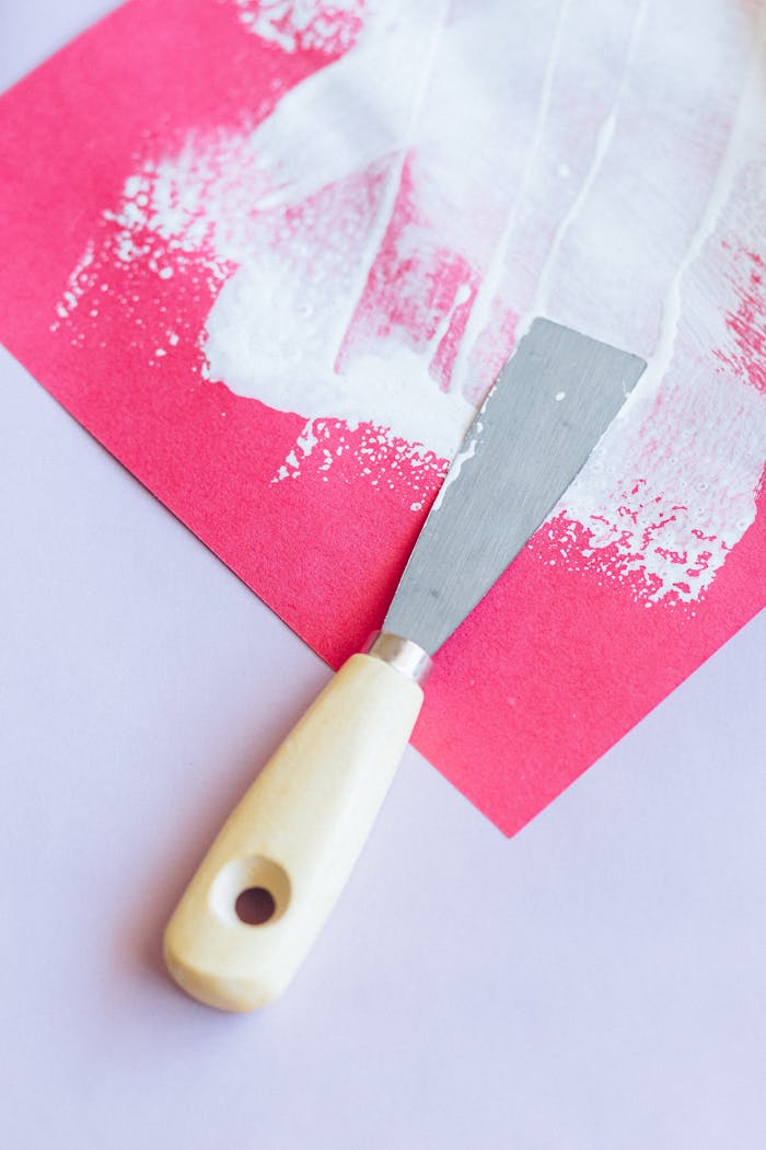 Palette knife spreading white paint on vibrant red paper for abstract art.